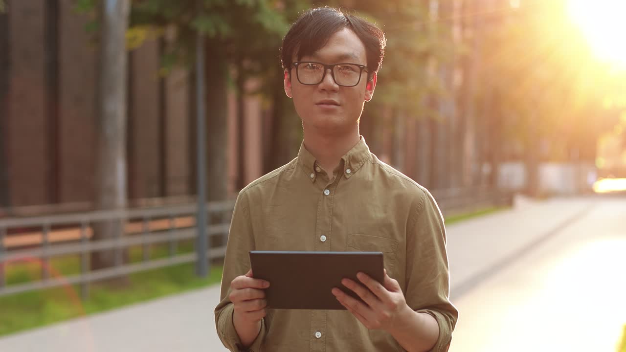 眼鏡をかけ、通りでタブレットを使用しているアジア人学生の男性