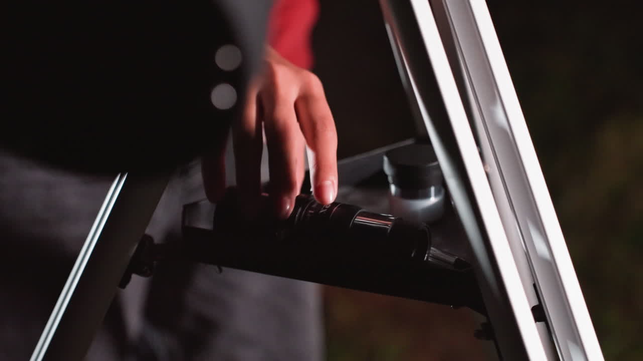 nighttime telescope setup hand adjusting shelf under dim backyard sky closeup on manual knob and eyepiece, slow deliberate movement, focused on precision and calm curiosity, subtle bokeh lights