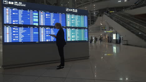 Woman-with-tablet-PC-by-flight-schedule-at-the-airport