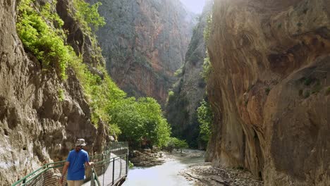 Tourist-on-safety-walkway-heads-into-steep-sided-sunlit-river-canyon-ravine