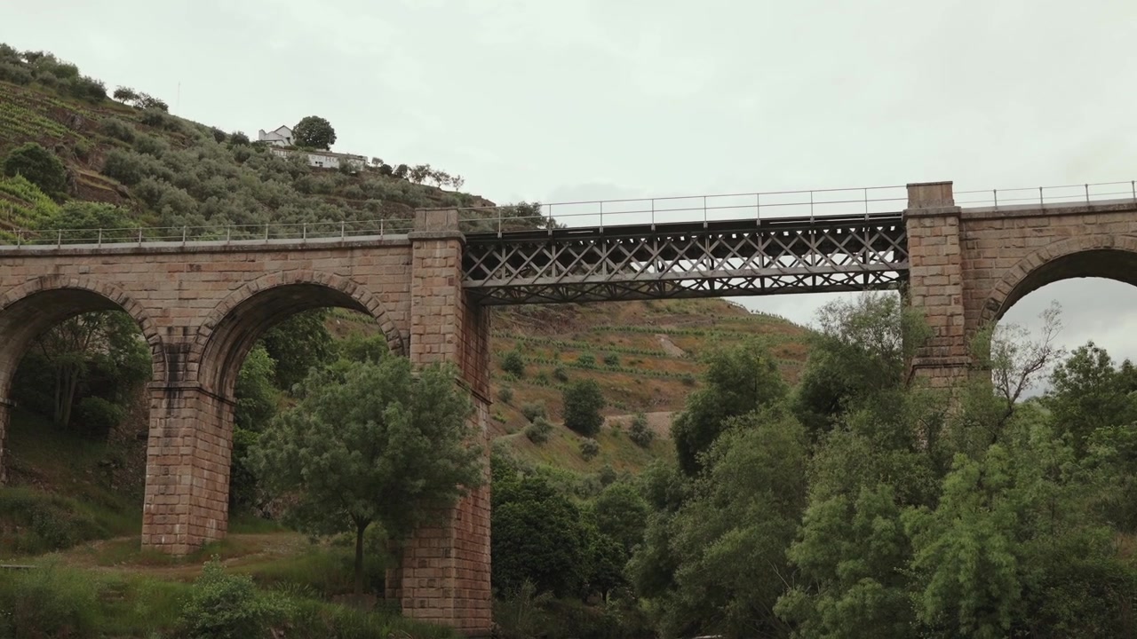 Storico viadotto ad arco in pietra con ponte ferroviario a traliccio metallico su una valle alberata nel Portogallo settentrionale.