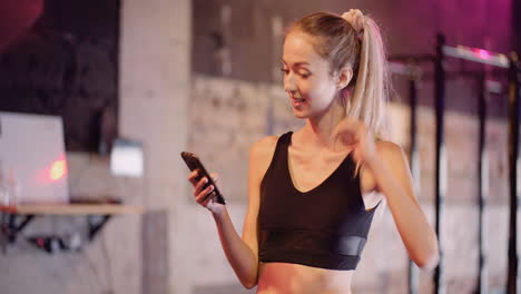 atractiva joven deportista enviando mensajes de texto a través del teléfono móvil durante el descanso en el gimnasio