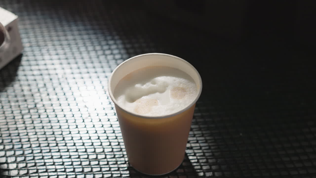 Close-up of a latte with foam art, featuring a simple design of a shape on top. The drink is in a paper cup with soft lighting, creating a calm atmosphere in a coffee shop or caf setting