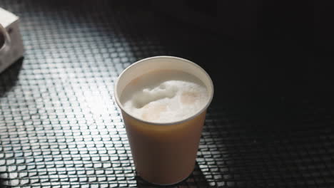 close-up of a latte with foam art, featuring a simple design of a shape on top. the drink is in a paper cup with soft lighting, creating a calm atmosphere in a coffee shop or caf setting
