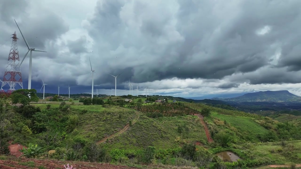Timelapse scenografico e drammatico di nuvole monsoniche scure che si muovono su un parco eolico a Phetchabun, Thailandia. Mostra enormi pale eoliche che generano energia rinnovabile su dolci crinali montuosi verdi