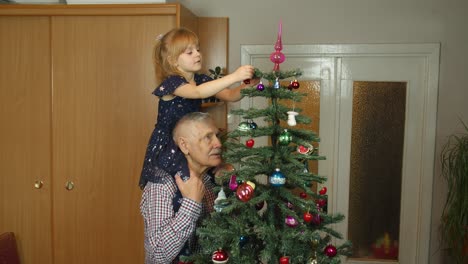 Kleines-Mädchen-Mit-Großen-Großeltern,-Die-Einen-Künstlichen-Weihnachtsbaum-Im-Altmodischen-Zuhause-Schmücken