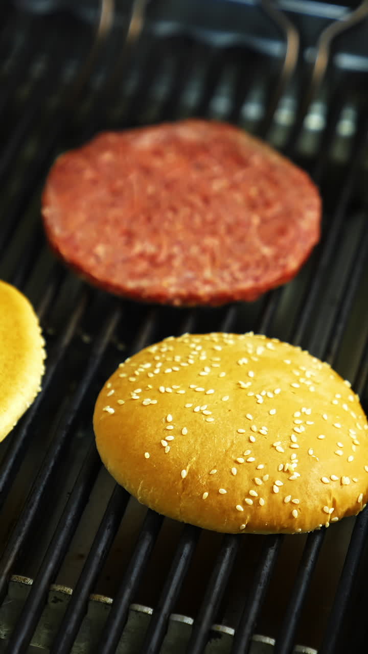 Two burger buns and one cutlet are being cooked on a barbecue grill. Delicious homemade burger. Vertical video