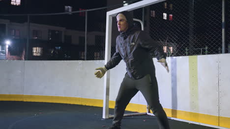 portero con ropa deportiva y guantes entrenando cerca del poste de la portería durante la sesión nocturna centrándose en las habilidades de captura y agilidad con un entorno urbano iluminado