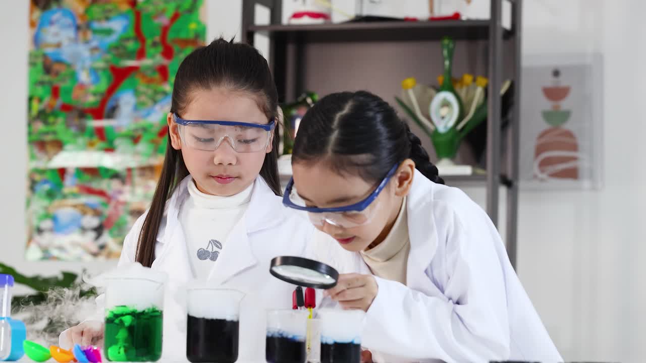 Siswi-siswi Asia mengenakan jas lab dan kacamata pelindung menggunakan kaca pembesar saat eksperimen sains