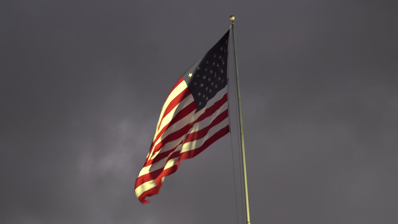 bandera patriótica de estados unidos ondeando a través de nubes oscuras que simbolizan la gloria, la fuerza, la resiliencia y la esperanza incluso en tiempos oscuros