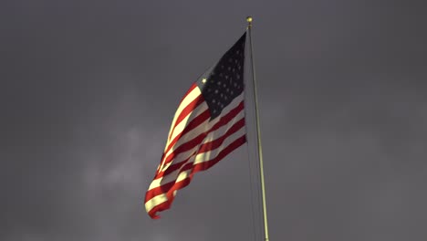 USA-Patriotic-flag-waving-through-dark-clouds-symbolizing-glory,-strength,-resilience,-and-hope-even-through-dark-times