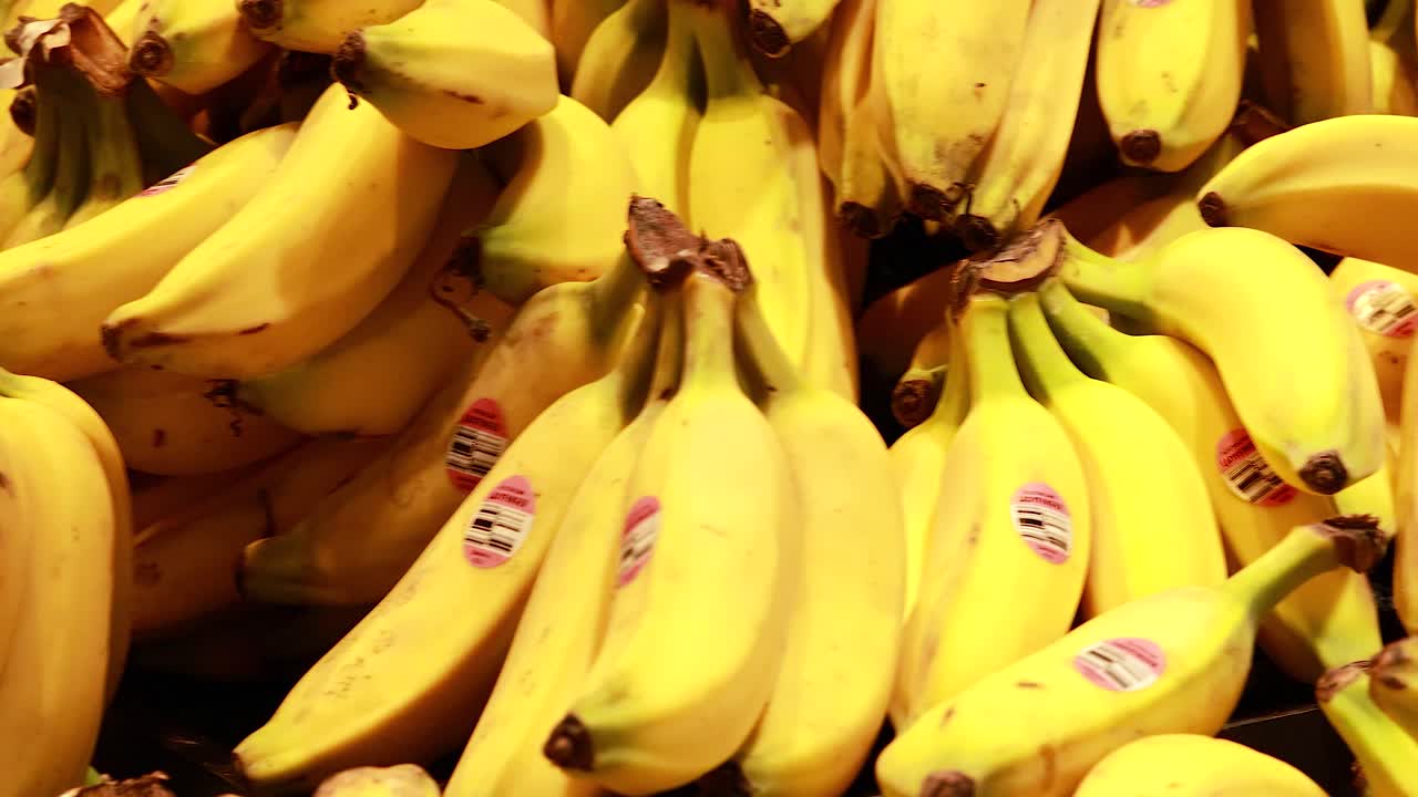 Bright yellow bananas stacked in a supermarket, under warm lighting, creating a vibrant and fresh atmosphere