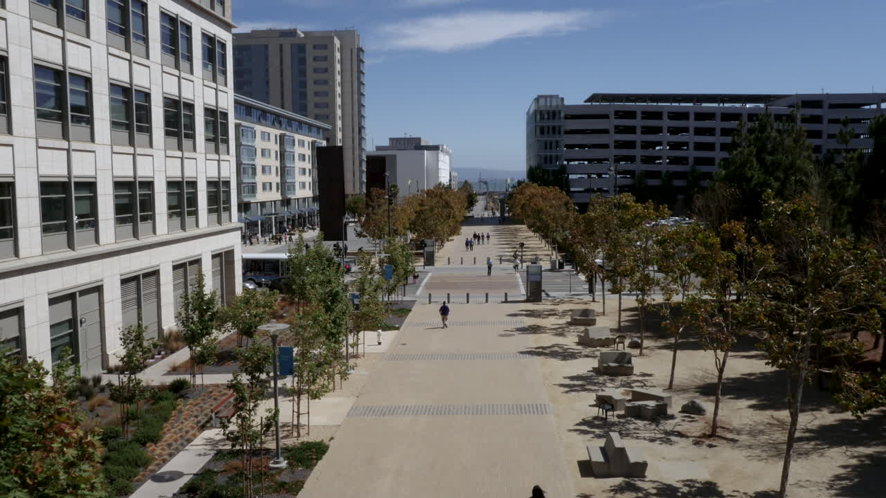 Vista diurna de um calçadão urbano moderno com pedestres e árvores.