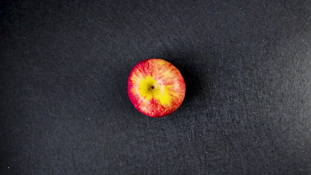 Rødt æble roterer langsomt på stedet mod en ren sort baggrund til isoleret produktbrug, set ovenfra.