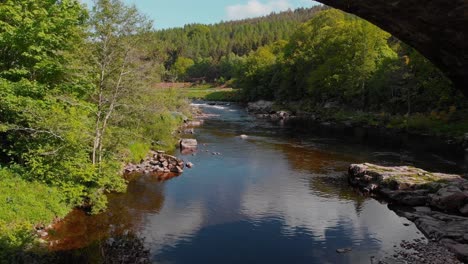 River-flowing-under-stone-bridge-arches-in-scottish-highlands,-drone