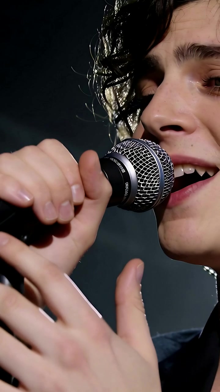 Video verticale: Cantante che inizia a cantare sul palco, posiziona il microfono per un passaggio potente, con auricolare e cappotto scuro