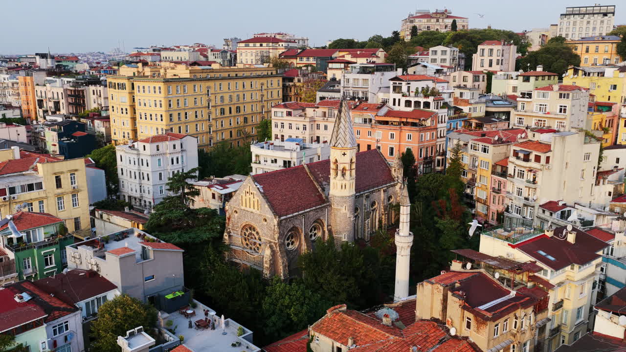 Close aerial view of a Gothic-style church with red rooftops and a slender minaret nearby, blending cultures in Istanbul’s heart