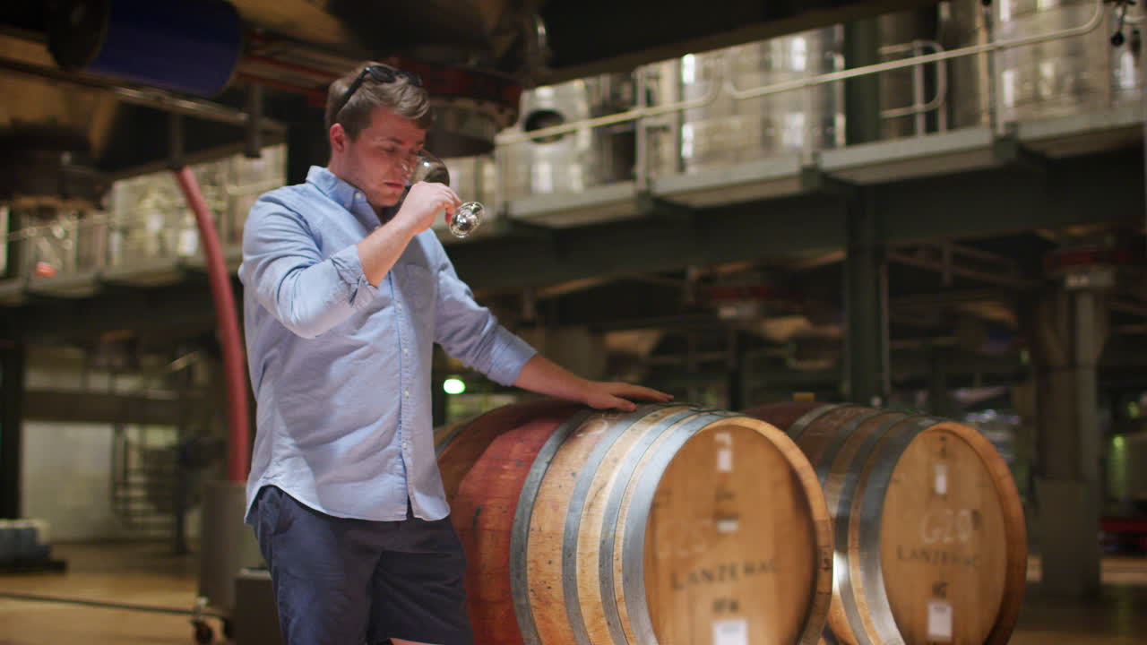 젊은 남자가 와인 공장 창고에서 와인을 맛보고 있다