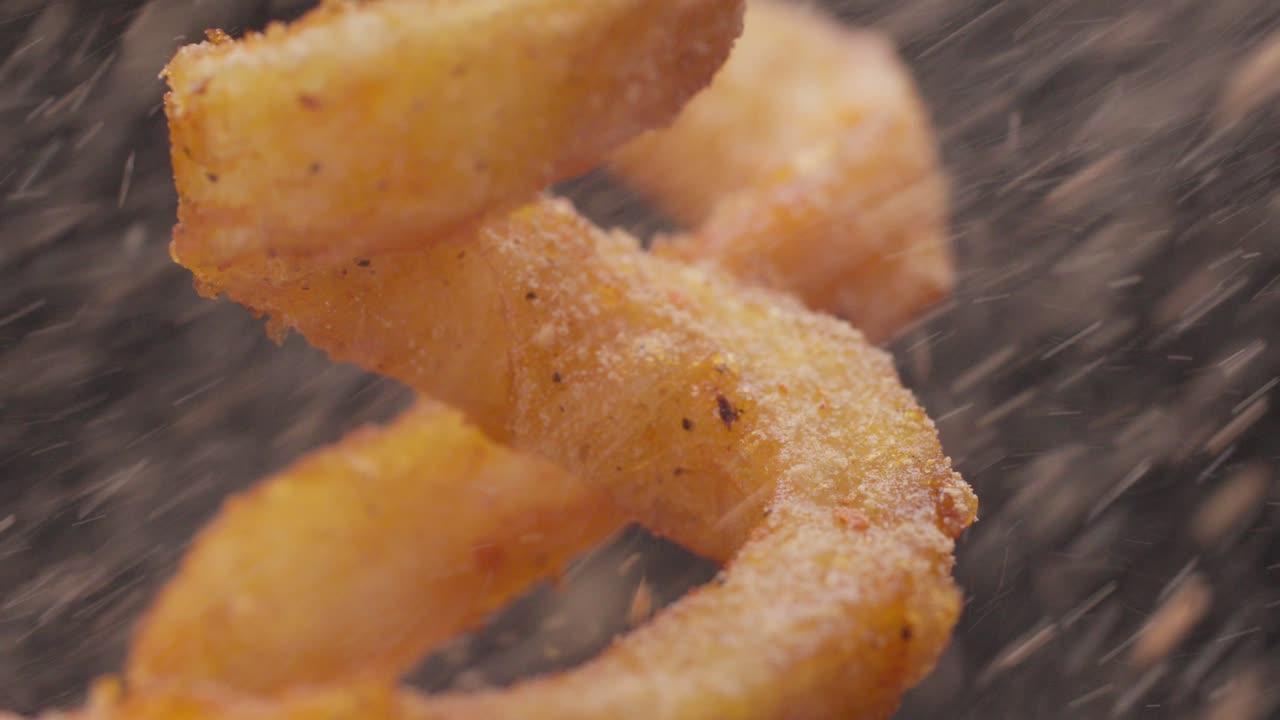 Slow motion macro shot of curly fries seasoned with spices