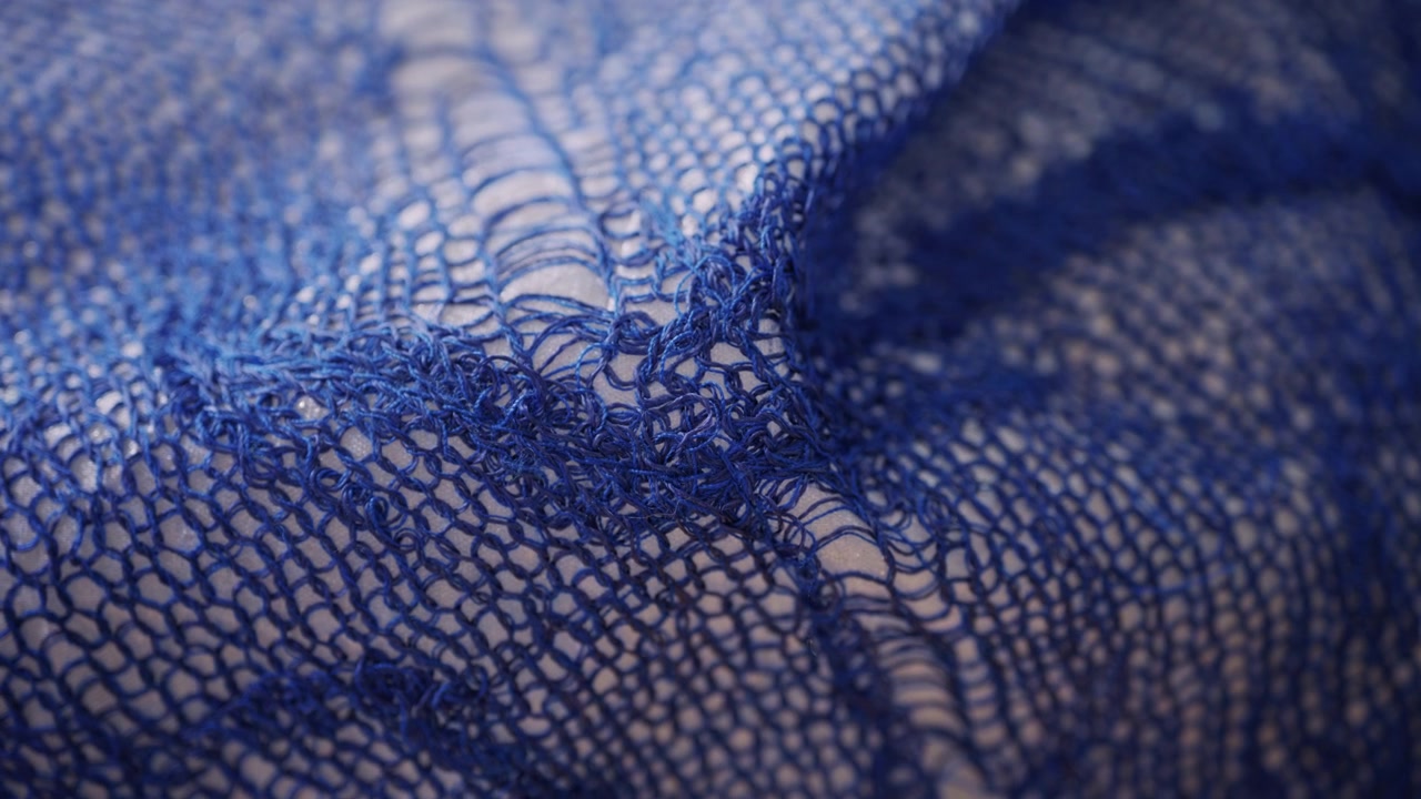 Close up of a blue openwork knitted textile stretched over a white form