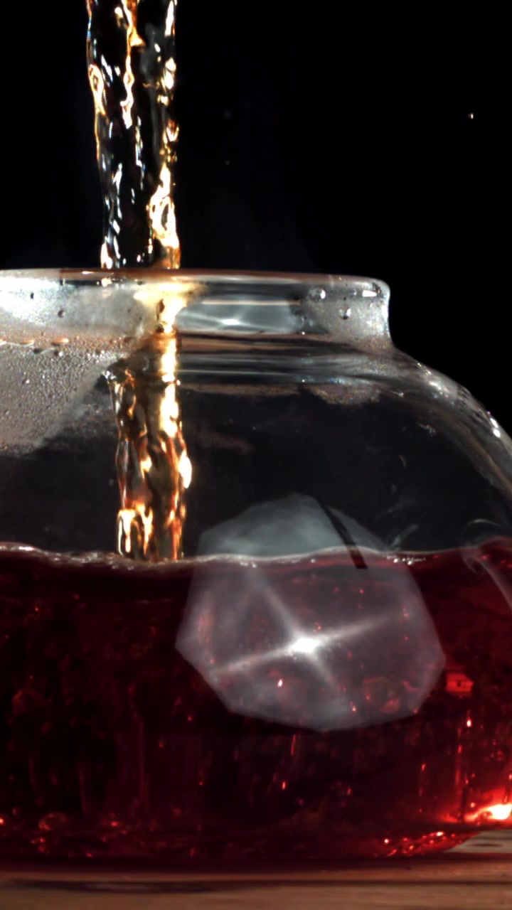 Versando liquido rosso in un bicchiere con ghiaccio su uno sfondo scuro