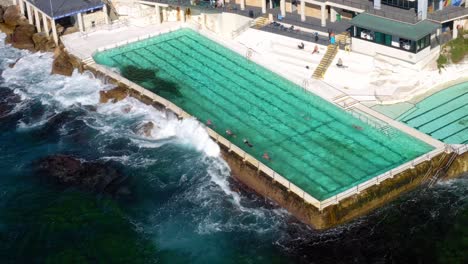 people swimming at bondi icebergs pool with strong waves crashing on side in bondi, nsw, australia