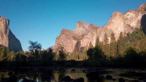 panning shot across towering granite peaks above a reflective mirror-like river