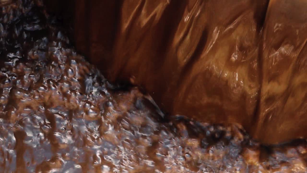 wastewater flowing over the edge of a treatment basin, showing dark liquid with a foamy, brown surface