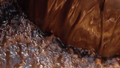 wastewater flowing over the edge of a treatment basin, showing dark liquid with a foamy, brown surface