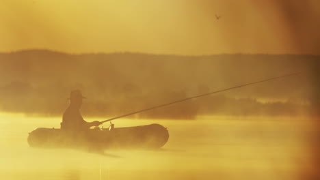 vista lejana de un anciano con sombrero en un barco pescando con una caña en el lago en una mañana nublada