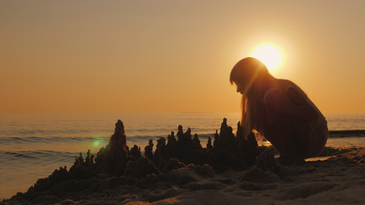 silueta de un niño construye un castillo de arena en la playa una hermosa puesta de sol 4k video