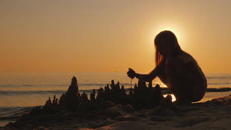 silhouette of a child builds a sand castle on the beach a beautiful sunset 4k video