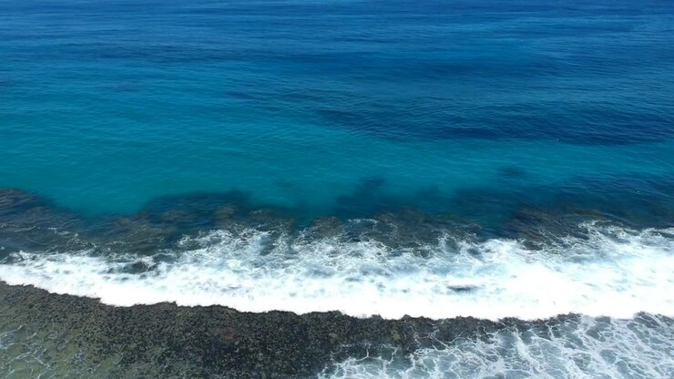 Ripresa aerea di onde che si infrangono sulla scogliera, mostrando un bel colore blu intenso dell'oceano.