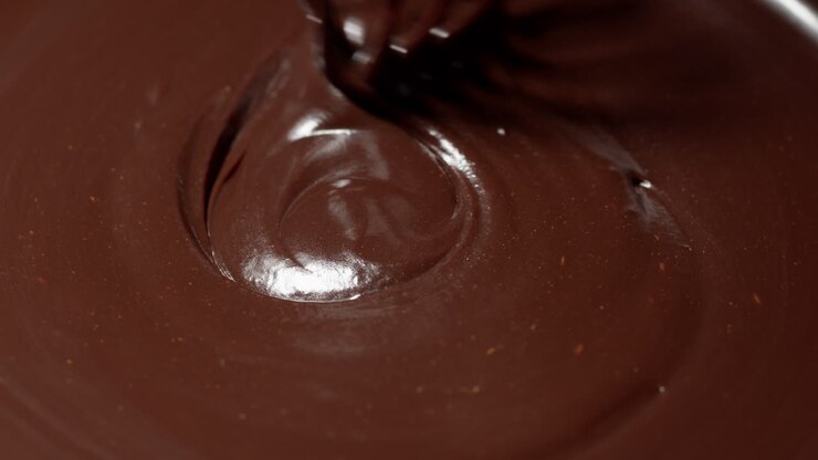 Chef che mescola cioccolato fondente liquido premium fuso con una frusta per la preparazione di caramelle fatte a mano