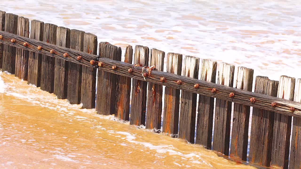 Wooden barrier along the Great Ocean Road with waves crashing against it, under bright daylight, showcasing dynamic ocean movement