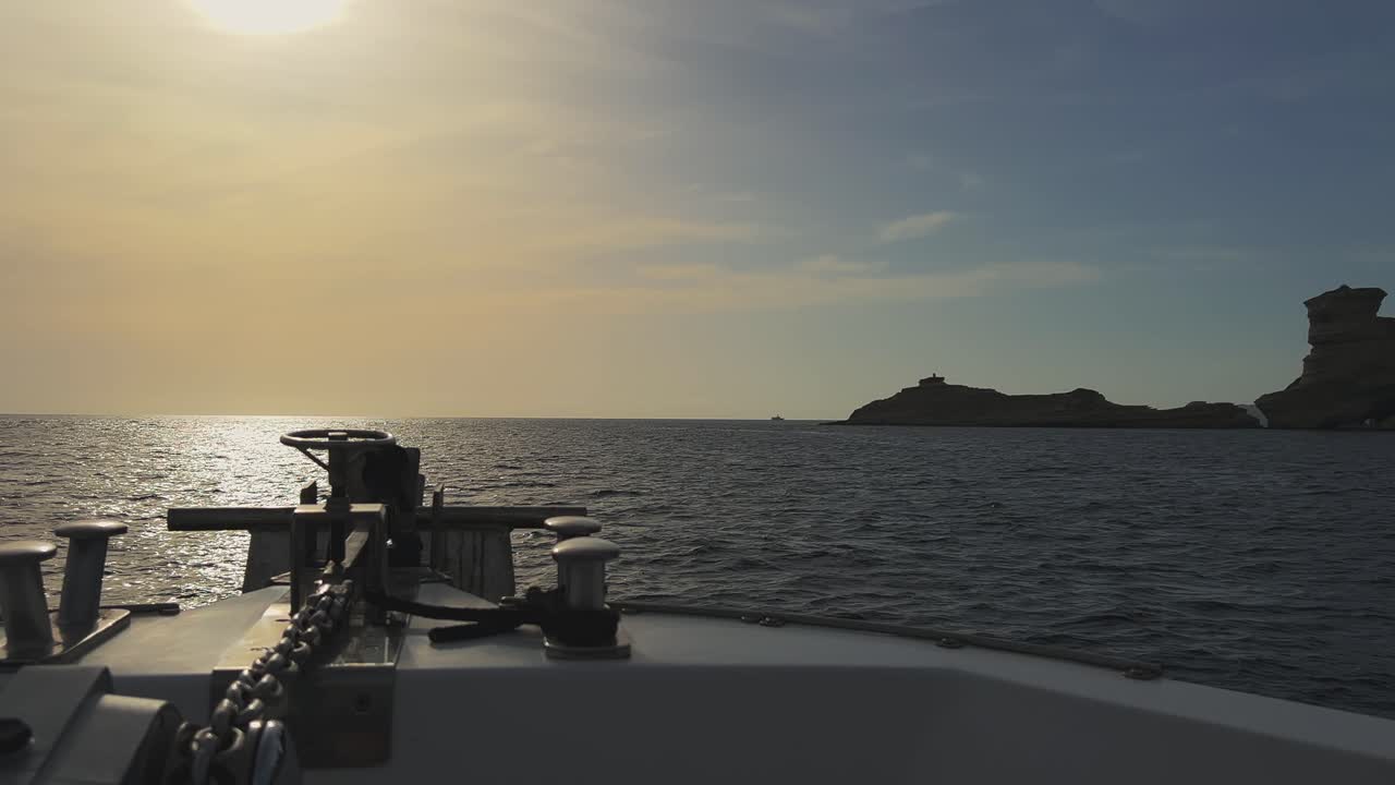 perspectiva desde la proa del barco de vela con el sol brillante en frente y los acantilados de la isla de córcega y el faro de capo pertusato en el fondo, francia