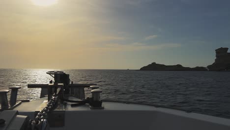 perspective from sailing boat bow with shining sun in front and corsica island cliffs and capo pertusato lighthouse in background, france