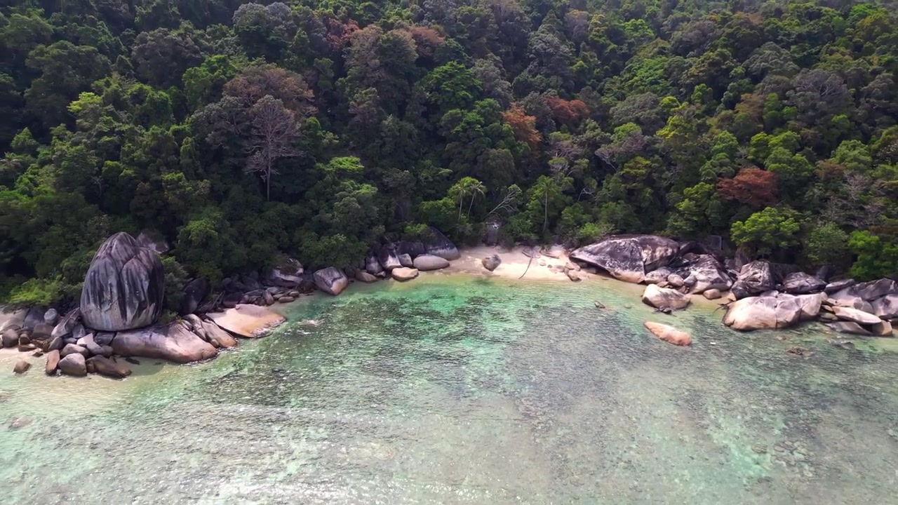 Turquoise water gently washing a sandy beach surrounded by granite rocks and lush tropical vegetation. Gorgeous aerial view flight drone shot footage from above