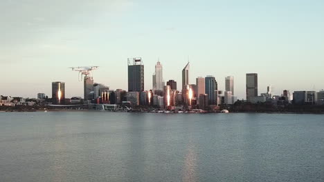 aerial tracking another drone flying sideways with water and cityscape in background