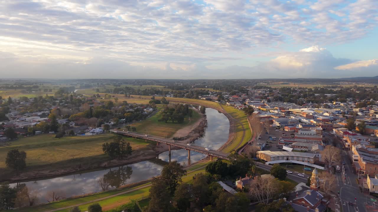 Drone aereo in orbita con bagliore dell'alba su città fluviale con ponte e tetti, atmosfera tranquilla, panoramica introduttiva di Maitland, Nuovo Galles del Sud, Australia