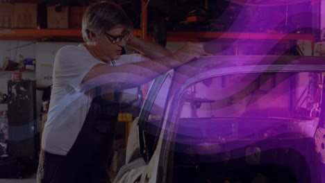 mechanic measuring car roof with phone on shoulder in repair shop, showing animated measuring lines
