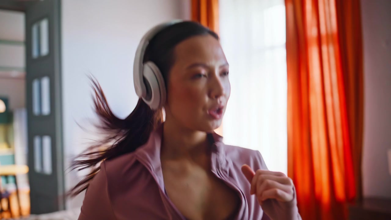 Donna energica che salta durante un allenamento cardio a casa. Ragazza asiatica che si allena con le cuffie.