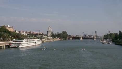 Overview of the Guadalquivir River in Seville, with a docked tourist cruise ship and people in canoes