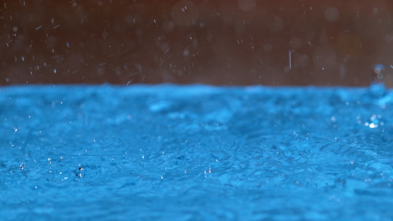 MACRO: Clear raindrops create a ripple effect on the surface of an empty pool.
