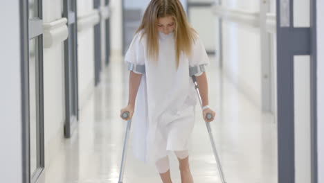 caucasian girl patient walking with crutches in hospital corridor, slow motion