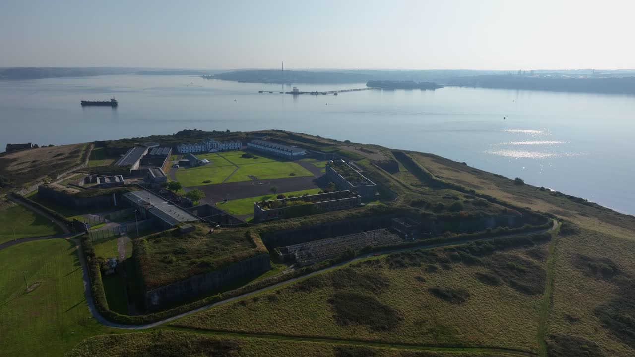 Spike Island, County Cork, Ireland, September 2024. Drone slow orbit clockwise above open waters, backlit sunlight over Corkbeg and Whitegate with walls and courtyard at center of historic prison.