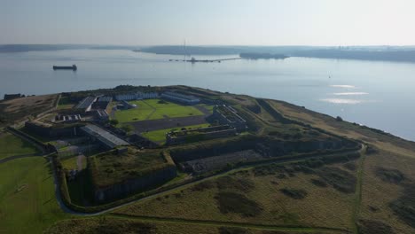 spike island, county cork, ireland, september 2024. drone slow orbit clockwise above open waters, backlit sunlight over corkbeg and whitegate with walls and courtyard at center of historic prison.