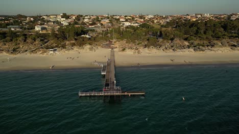 Aerial-establishing-shot-of-people-on-jetty-at-Coogee-Beach-in-Perth-City-during-golden-sunset-time,-Western-Australia---Drone-orbiting-shot