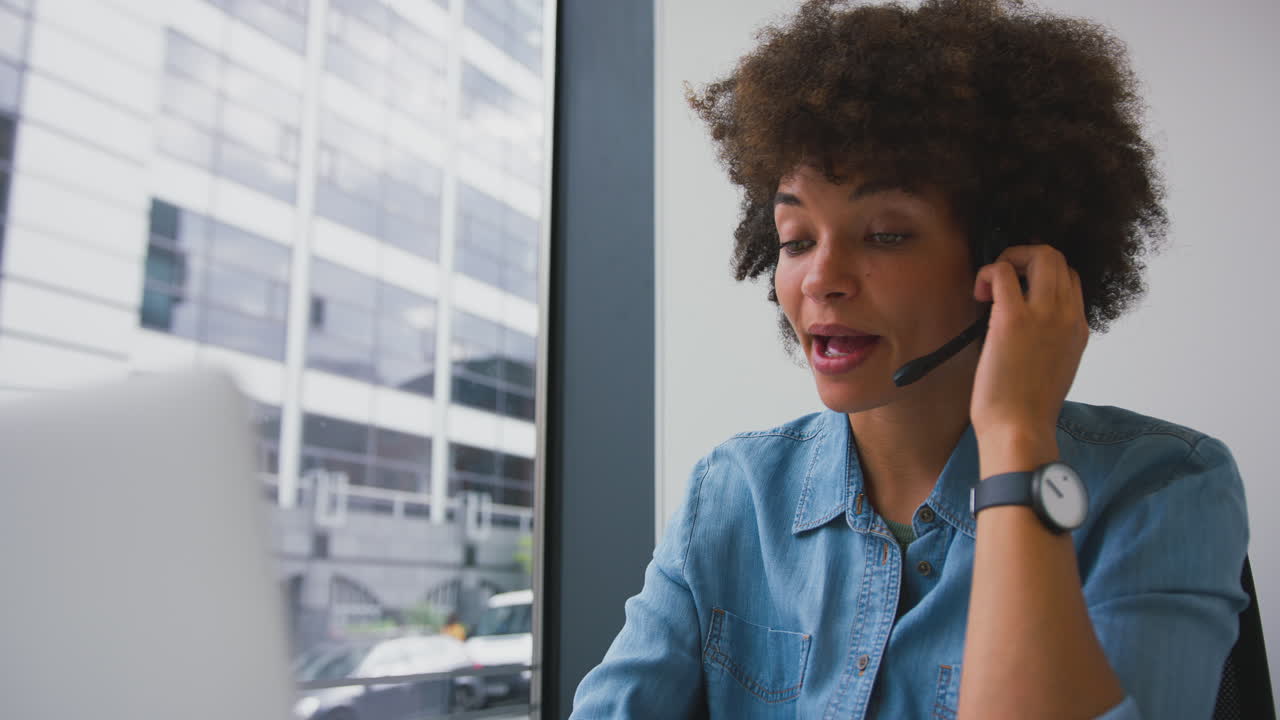 Young Businesswoman In Modern Office Working On Laptop Using Wireless Headset
