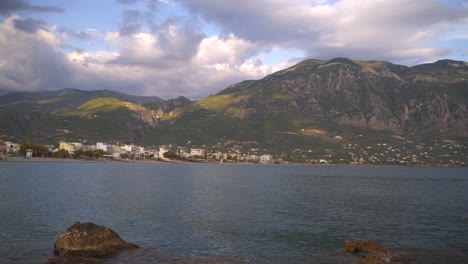 wide panoramic view of east side of kalamata, view from pier on a cloudy spring afternoon . sea and rocks in foreground, taygetos mountain on background , 4k pan footage